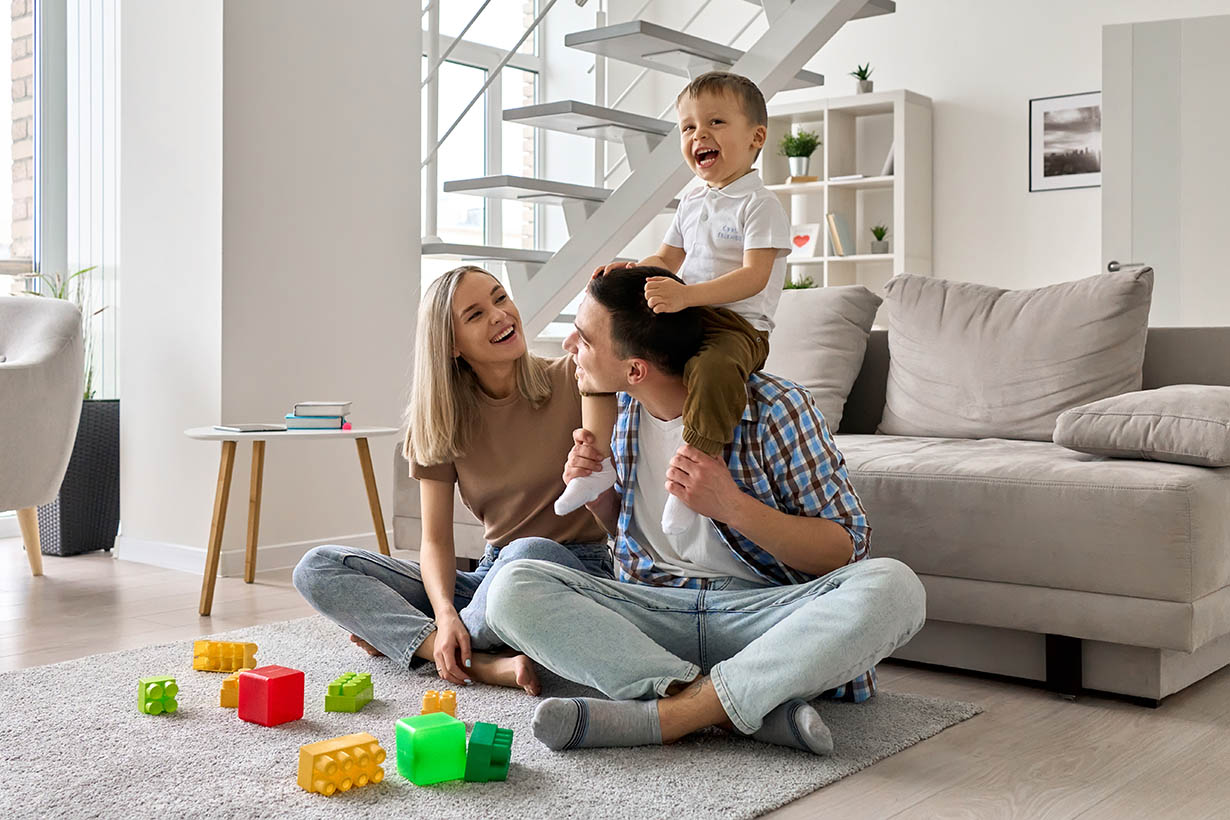 Happy young family couple having fun playing with happy cute kid sitting on dad's shoulders in modern living room